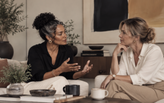 Two women talking on a sofa over coffee in a calm living room, having an open conversation about menopause